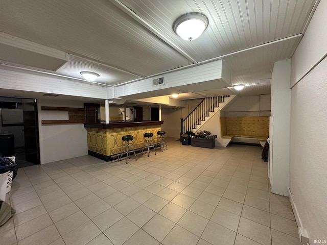 finished basement featuring a dry bar, visible vents, stairway, and light tile patterned flooring