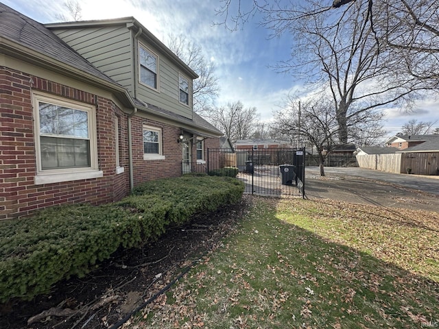 view of side of home featuring brick siding, fence, and roof with shingles