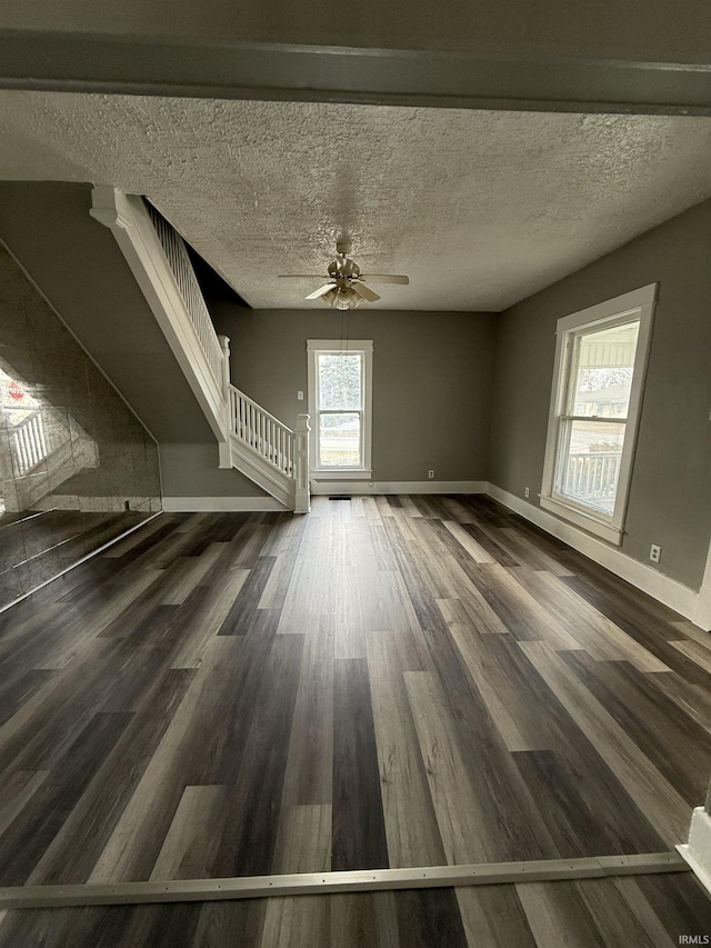 unfurnished living room featuring baseboards, a textured ceiling, stairway, and wood finished floors