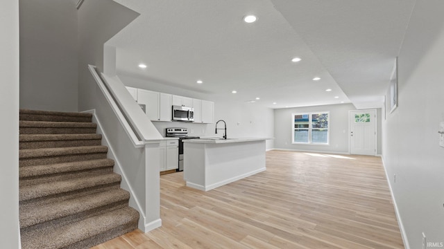 kitchen with open floor plan, stainless steel appliances, light wood-type flooring, and white cabinetry