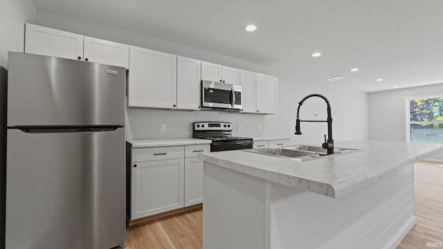 kitchen featuring light wood-style flooring, appliances with stainless steel finishes, a kitchen island with sink, white cabinets, and a sink