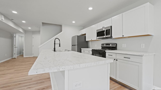 kitchen featuring a kitchen island with sink, light wood-style flooring, stainless steel appliances, a sink, and white cabinetry