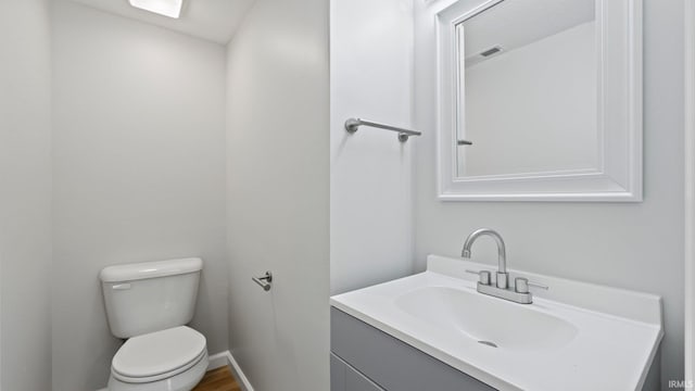 bathroom featuring visible vents, toilet, vanity, wood finished floors, and baseboards