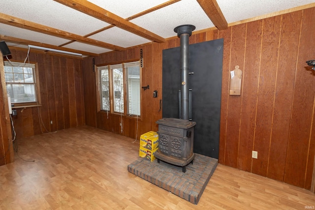 unfurnished living room featuring a wealth of natural light, wood walls, wood finished floors, and a wood stove