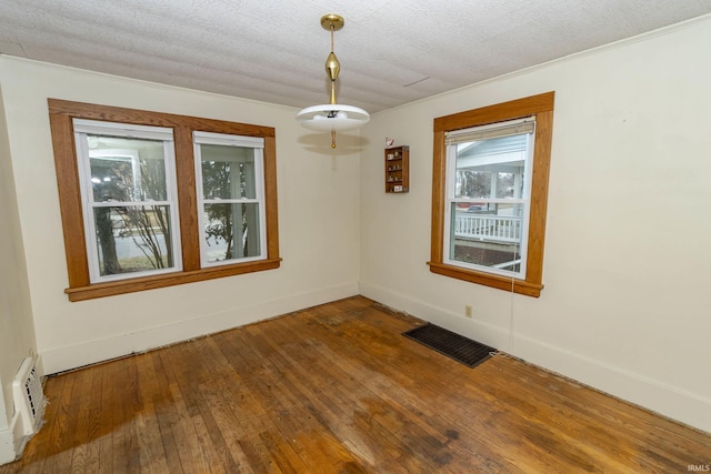 unfurnished room with wood-type flooring, visible vents, a textured ceiling, and baseboards