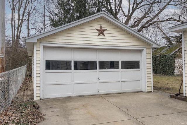 detached garage featuring concrete driveway and fence