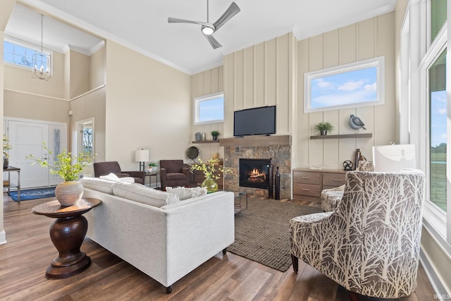 living area with ornamental molding, a wealth of natural light, a stone fireplace, and wood finished floors