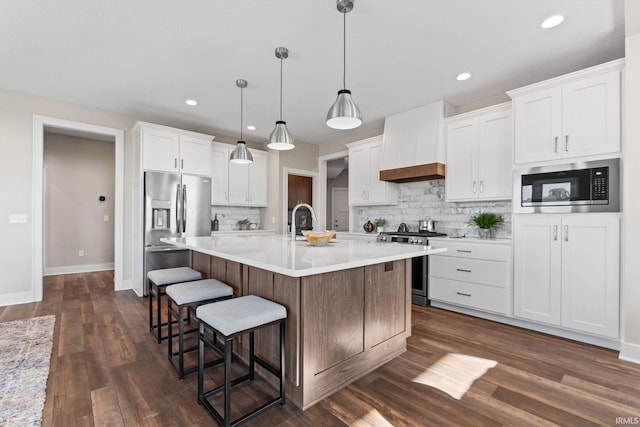 kitchen with white cabinets, custom range hood, appliances with stainless steel finishes, a kitchen breakfast bar, and light countertops