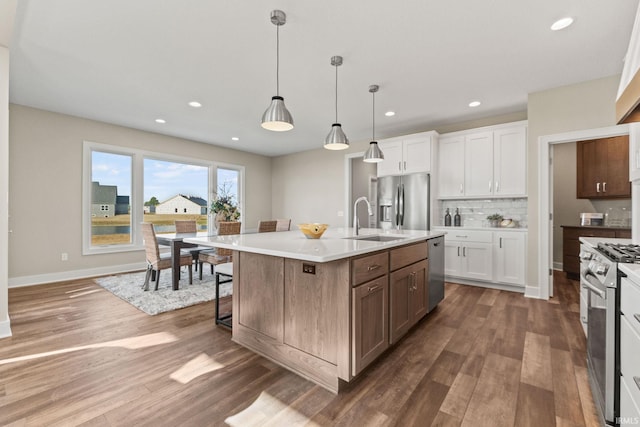 kitchen featuring stainless steel appliances, wood finished floors, a sink, white cabinets, and decorative backsplash