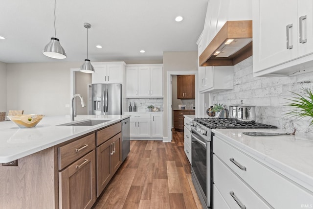 kitchen with white cabinets, appliances with stainless steel finishes, wood finished floors, wall chimney range hood, and a sink