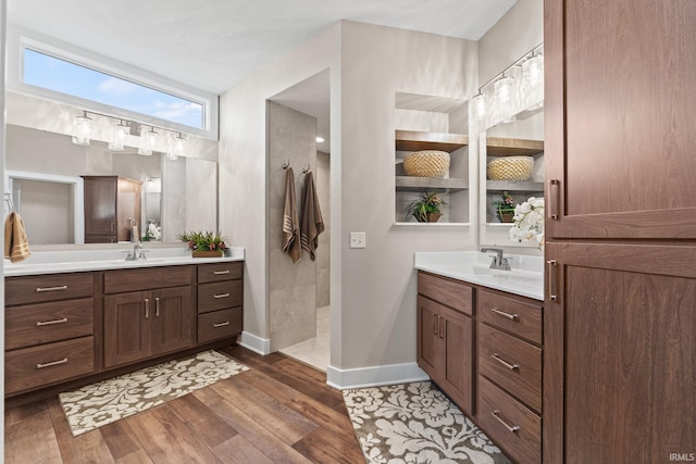 full bathroom featuring a sink, wood finished floors, walk in shower, and two vanities