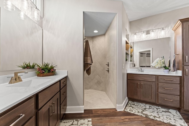 bathroom with two vanities, a walk in shower, a sink, and wood finished floors