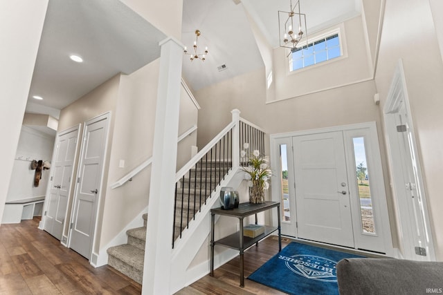 entryway with recessed lighting, a notable chandelier, wood finished floors, a towering ceiling, and stairs