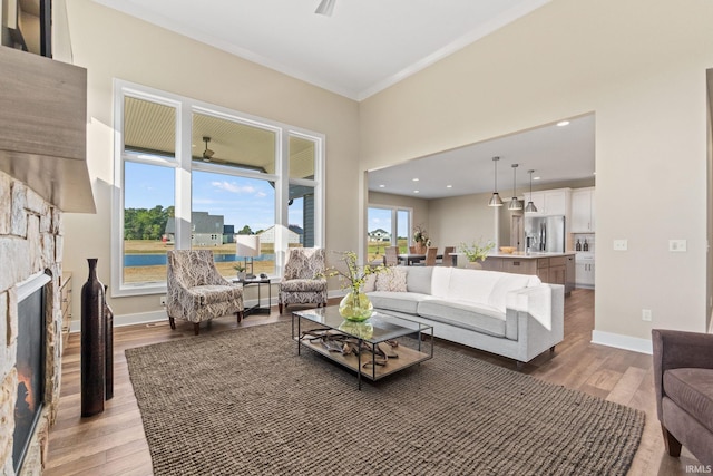 living room with light wood-style floors, a fireplace, baseboards, and a ceiling fan