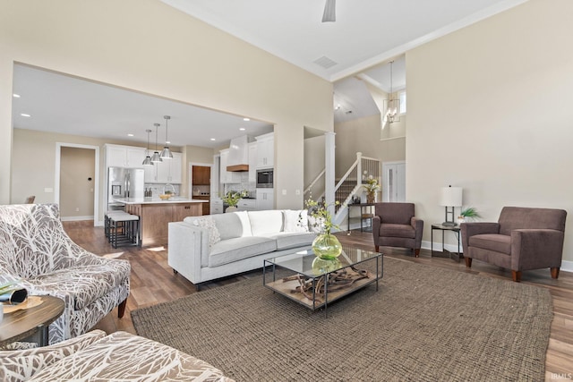 living room with a high ceiling, wood finished floors, visible vents, baseboards, and stairway