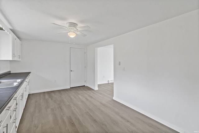 interior space featuring wood finished floors, a sink, a ceiling fan, and baseboards