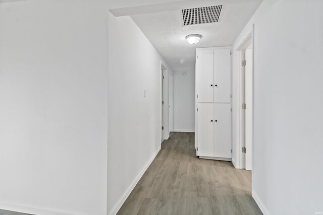 corridor with light wood-style floors, visible vents, and baseboards