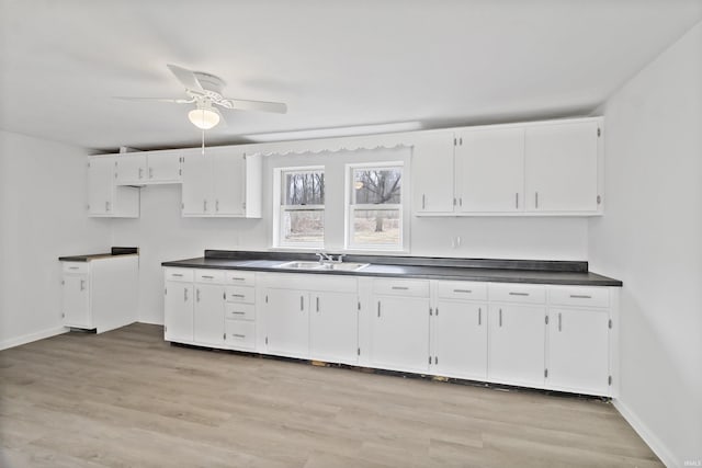 kitchen with dark countertops, light wood-style floors, white cabinets, and a sink