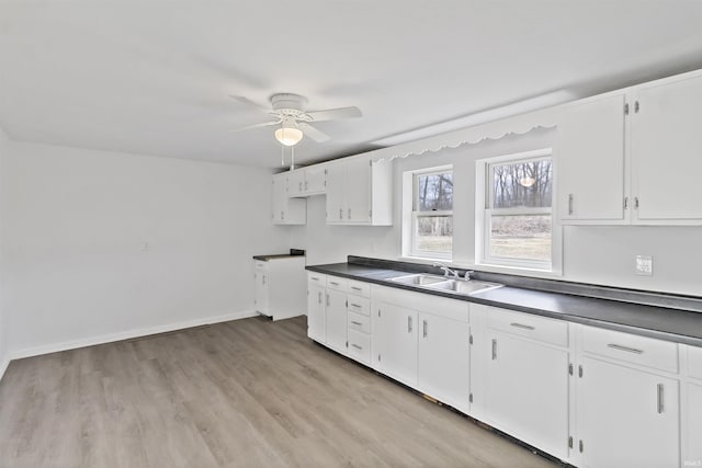 kitchen with dark countertops, light wood-style floors, white cabinetry, a sink, and ceiling fan