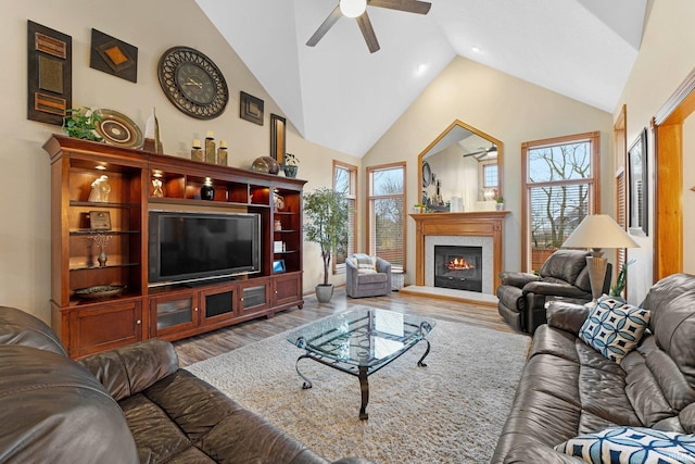 living area with high vaulted ceiling, a ceiling fan, wood finished floors, and a glass covered fireplace