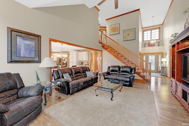 living room featuring a towering ceiling, stairs, ornamental molding, light wood-type flooring, and an inviting chandelier