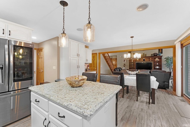 kitchen with white cabinetry, a center island, light wood finished floors, stainless steel fridge, and pendant lighting