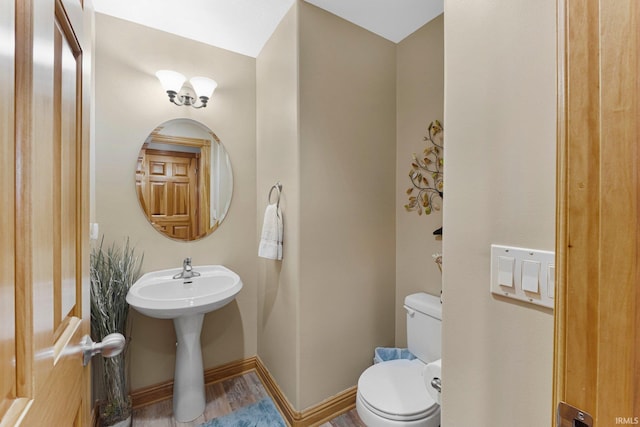 half bath with baseboards, toilet, and wood finished floors