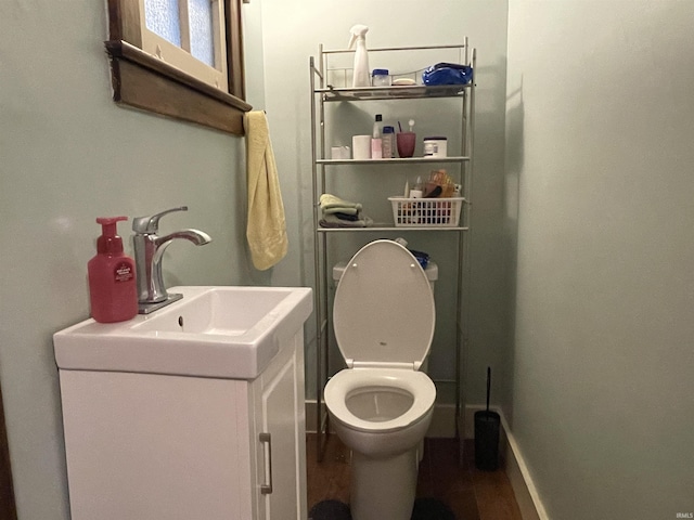 half bath featuring toilet, baseboards, wood finished floors, and vanity