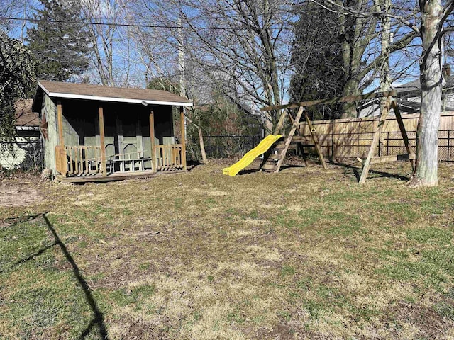 view of yard with a fenced backyard, an outdoor structure, a playground, and a storage unit