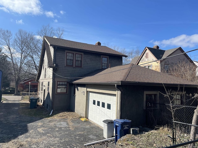 view of side of home featuring driveway, a shingled roof, a chimney, and an attached garage