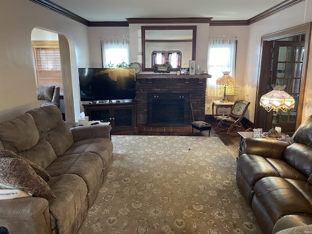 living room featuring arched walkways, a brick fireplace, crown molding, and wood finished floors