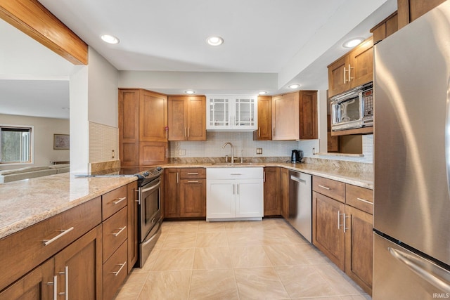 kitchen with brown cabinetry, light stone counters, stainless steel appliances, and a sink