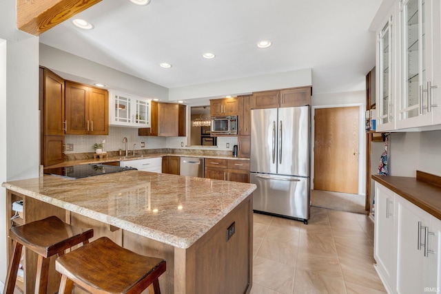 kitchen featuring brown cabinets, appliances with stainless steel finishes, glass insert cabinets, light stone countertops, and a peninsula