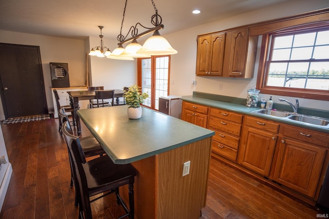 kitchen featuring dark wood-type flooring, a center island, brown cabinetry, and a sink