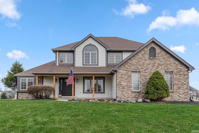 view of front of property with a shingled roof, a front yard, and brick siding