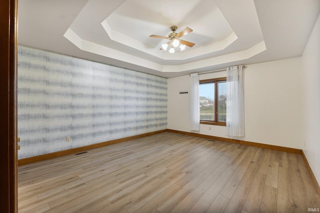 empty room with a raised ceiling, visible vents, a ceiling fan, wood finished floors, and baseboards