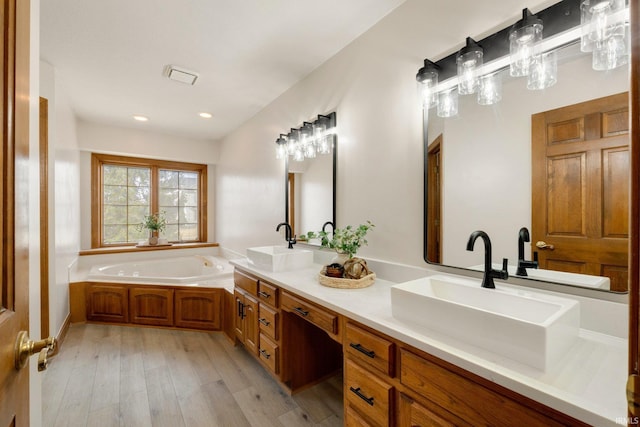 bathroom with double vanity, a garden tub, a sink, and wood finished floors