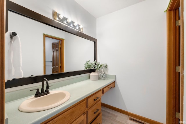 bathroom with visible vents, vanity, baseboards, and wood finished floors