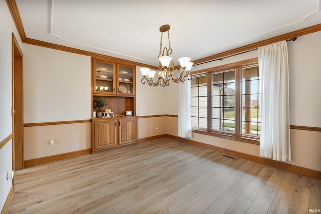 unfurnished dining area with light wood finished floors, baseboards, visible vents, ornamental molding, and a chandelier