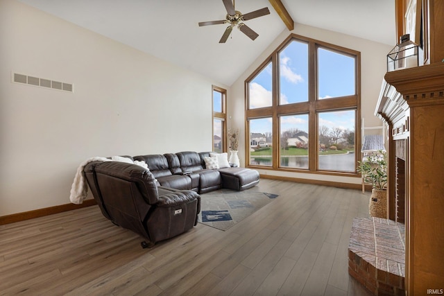 living area with visible vents, wood finished floors, a brick fireplace, high vaulted ceiling, and beam ceiling