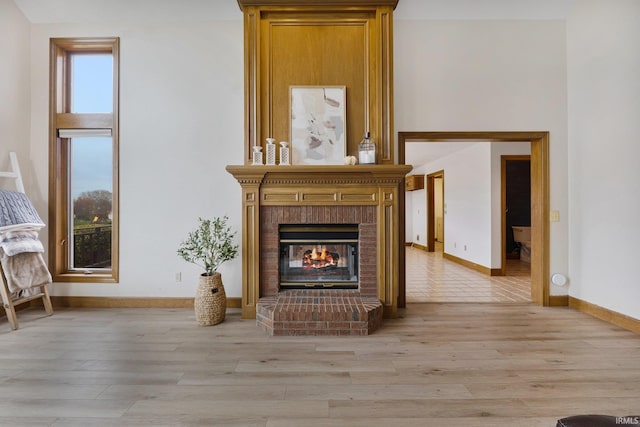 unfurnished living room with a brick fireplace, baseboards, and light wood finished floors