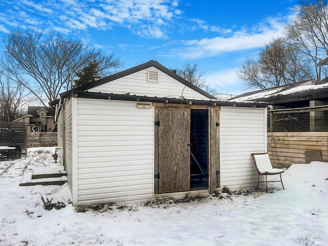 snow covered structure with fence and an outbuilding