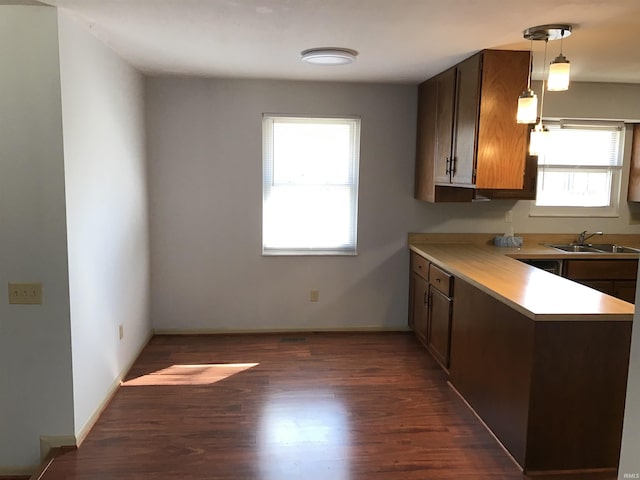 kitchen with baseboards, wood finished floors, hanging light fixtures, light countertops, and a sink