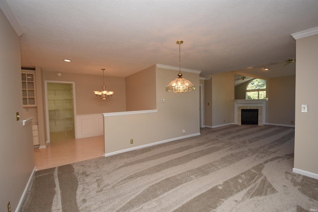 unfurnished living room with light carpet, crown molding, a tiled fireplace, and an inviting chandelier