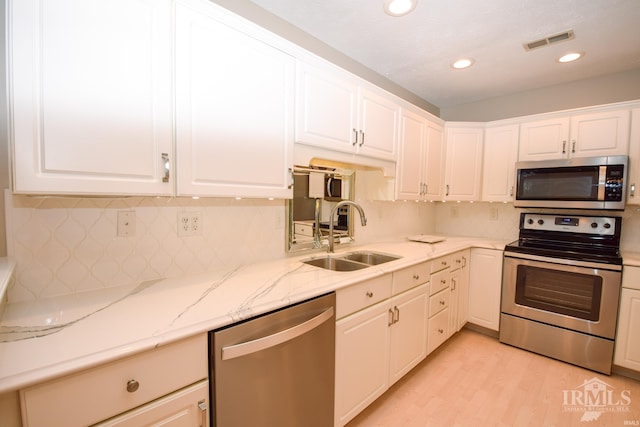 kitchen with visible vents, appliances with stainless steel finishes, light stone countertops, white cabinetry, and a sink