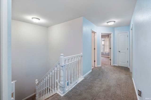 hall featuring carpet floors, baseboards, and an upstairs landing