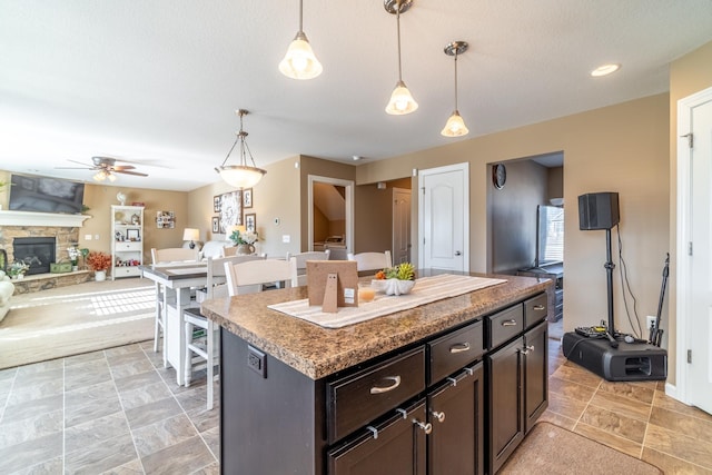 kitchen featuring a kitchen island, stone finish floor, open floor plan, hanging light fixtures, and a stone fireplace