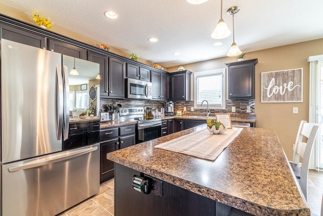 kitchen with stainless steel appliances, dark countertops, tasteful backsplash, hanging light fixtures, and a sink