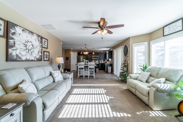 living room featuring light carpet, ceiling fan, visible vents, and a textured ceiling