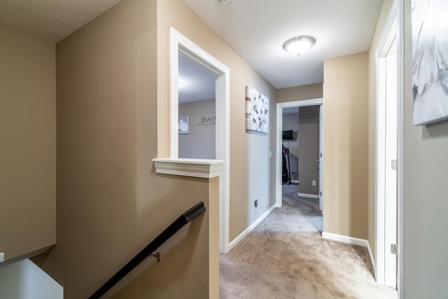 hallway with baseboards, light colored carpet, a textured ceiling, and an upstairs landing